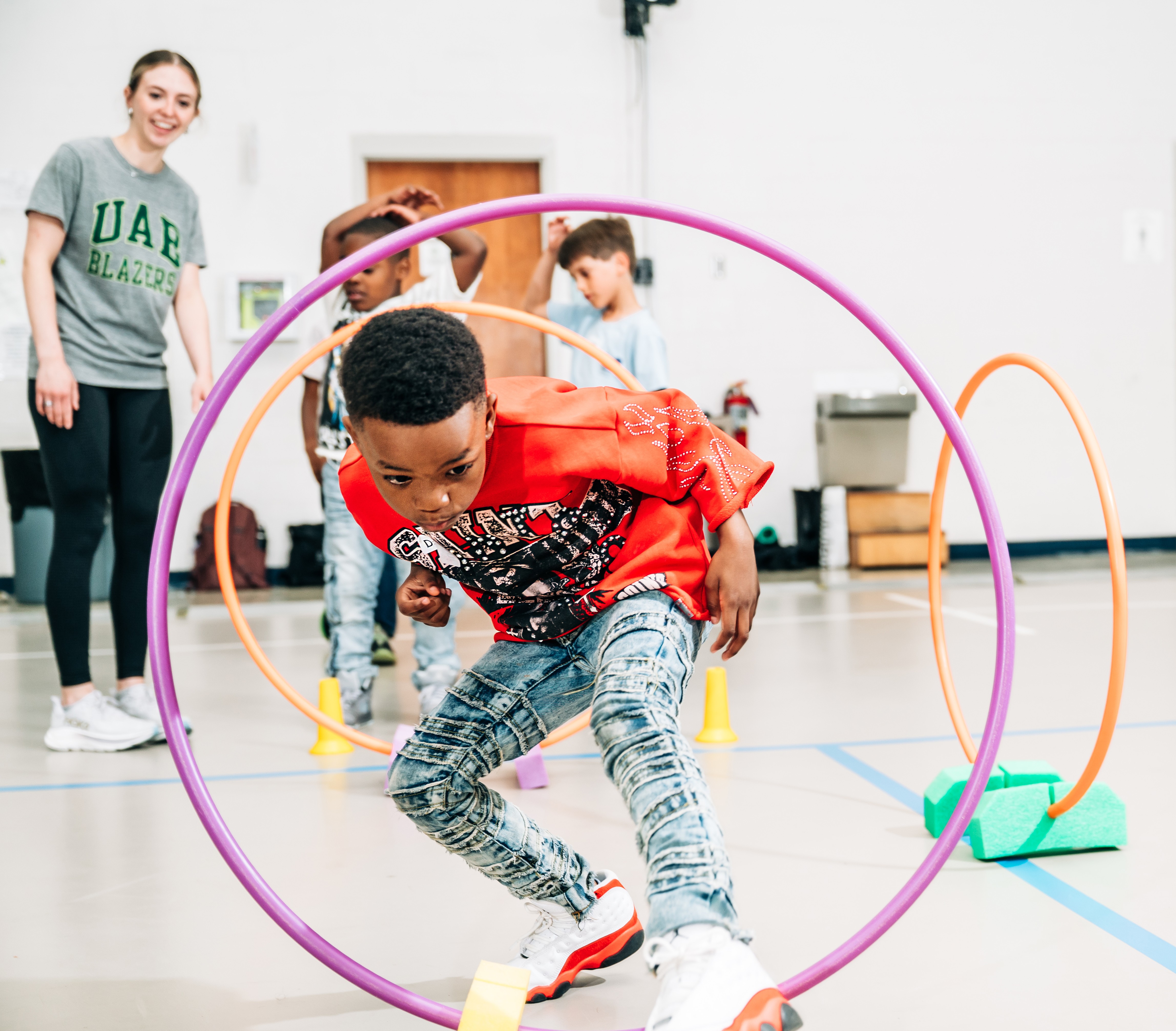 Kids running through hoops as an instructor looks on.